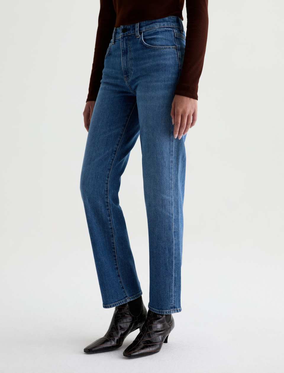 Angled front view of the AG Jeans Brinley Mid-Rise Jean in Chord on a model, showing the faded wash and leg shape.