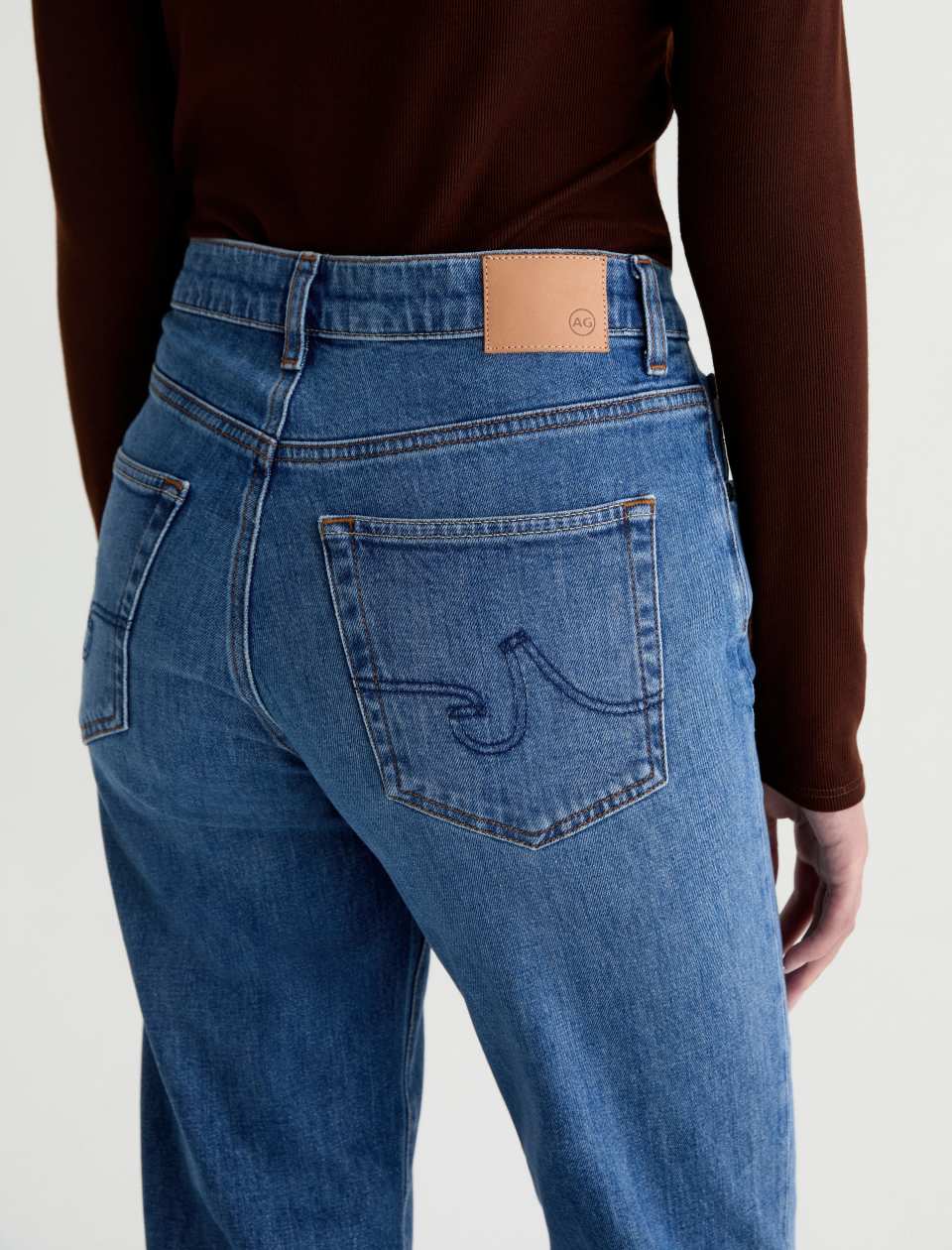 Close-up of the AG Jeans Brinley Mid-Rise Jean in Chord on a model, showing the embroidered back pocket and tan AG waistband patch.