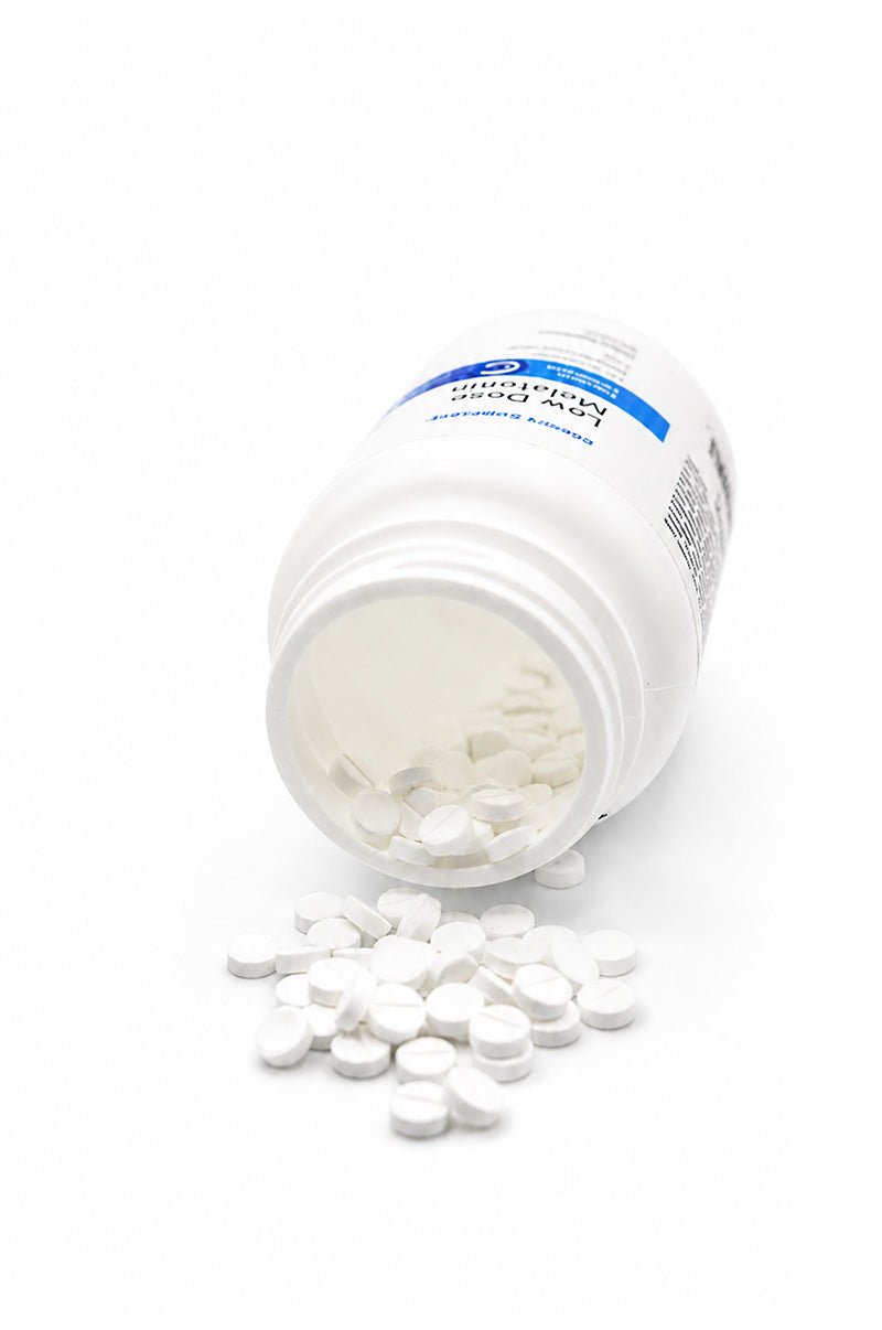 White tablets spilling out of a bottle of Cooper Complete Low Dose Melatonin 1mg supplements.