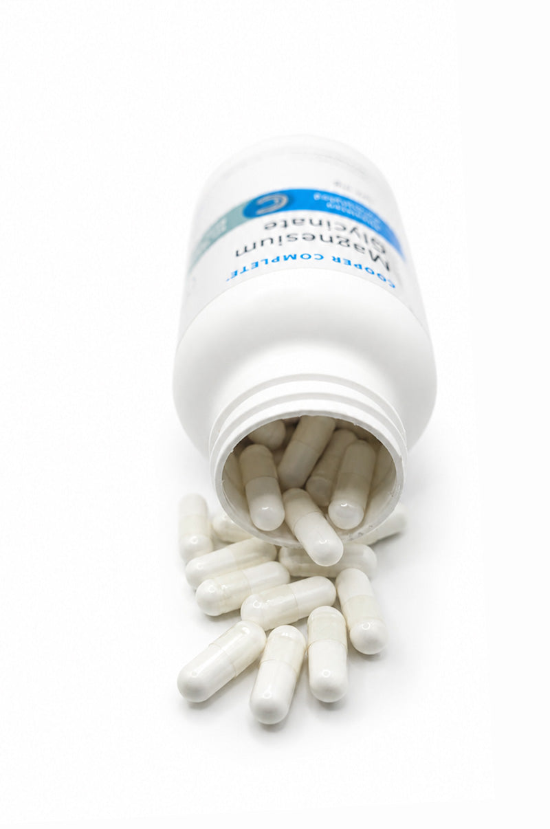 Open white Cooper Complete Magnesium Glycinate Supplement pill bottle with capsules spilling out on a white background