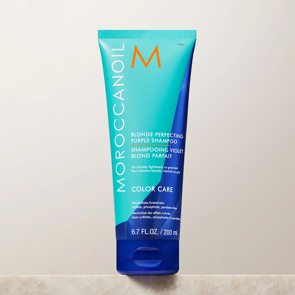 Turquoise and blue tube of Moroccanoil Blonde Perfecting Purple Shampoo to help neutralize craziness in blonde, lightened, or gray hair, 6.7 fl oz.