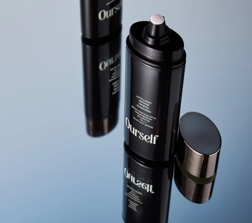 Two black squeeze bottles of Ourself Intelligent Defense Mineral Sunscreen on reflective surface. 
