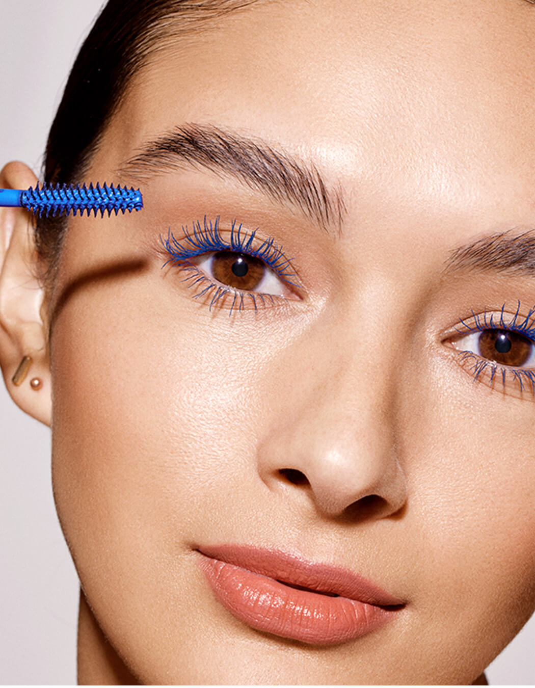 Close up of model applying RevitaLash Double-Ended blue Volumizing Primer to bare lashes beginning at the base of the eyelash to prep lashes. 