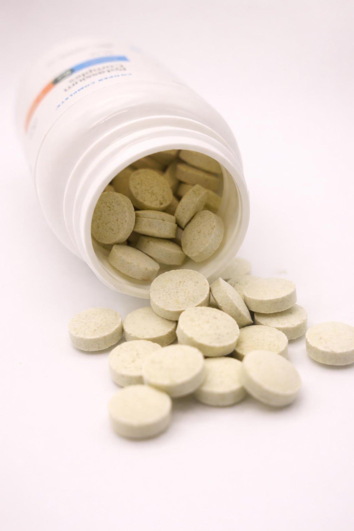 Open white Cooper Complete Potassium Complex pill bottle with tablets spilling out on a white background