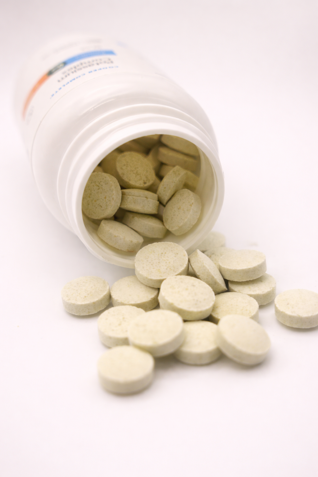Open white Cooper Complete Potassium Complex pill bottle with tablets spilling out on a white background
