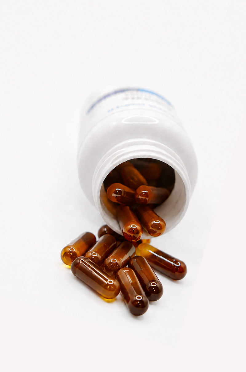 Open white Cooper Complete Prostate Health Supplement pill bottle with liquid capsules spilling out on a white background