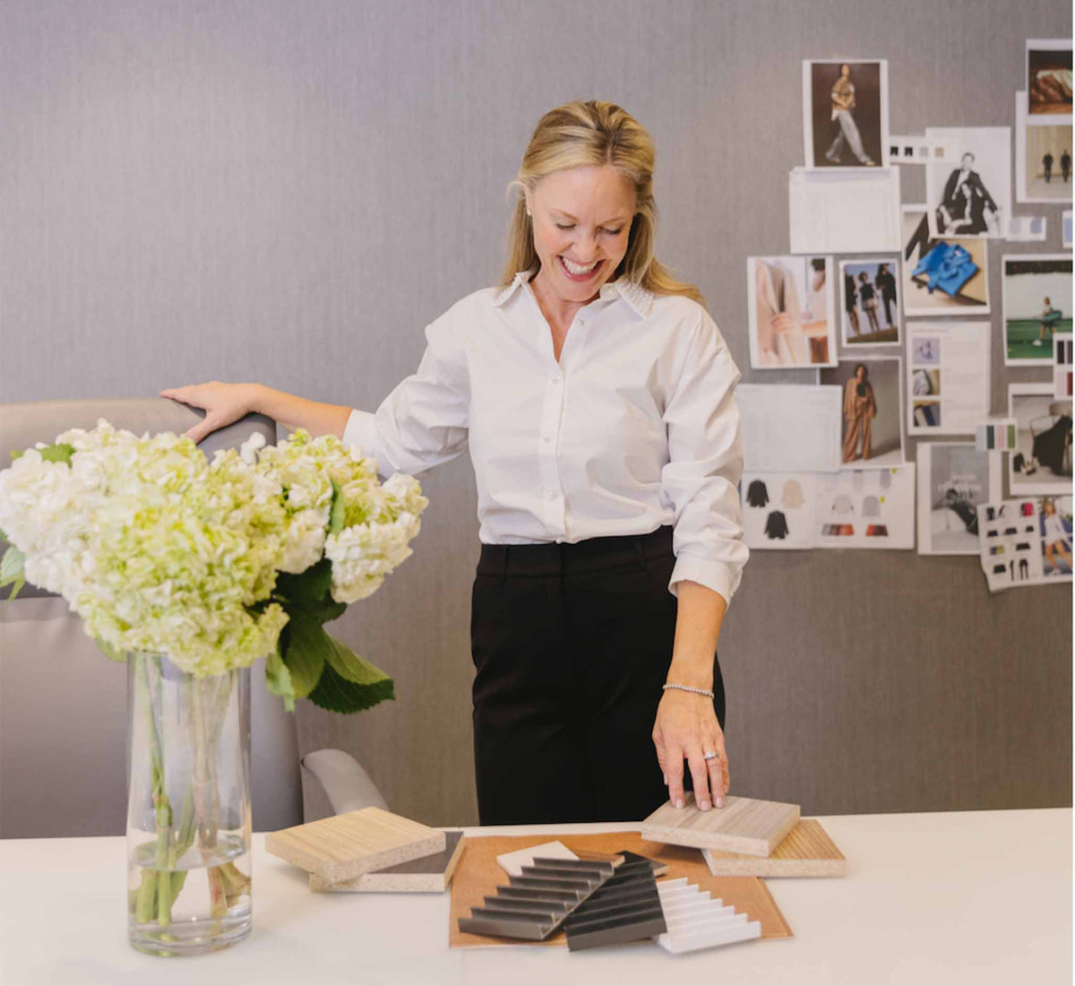 Smiling woman standing in design studio with swatches and flowers. 