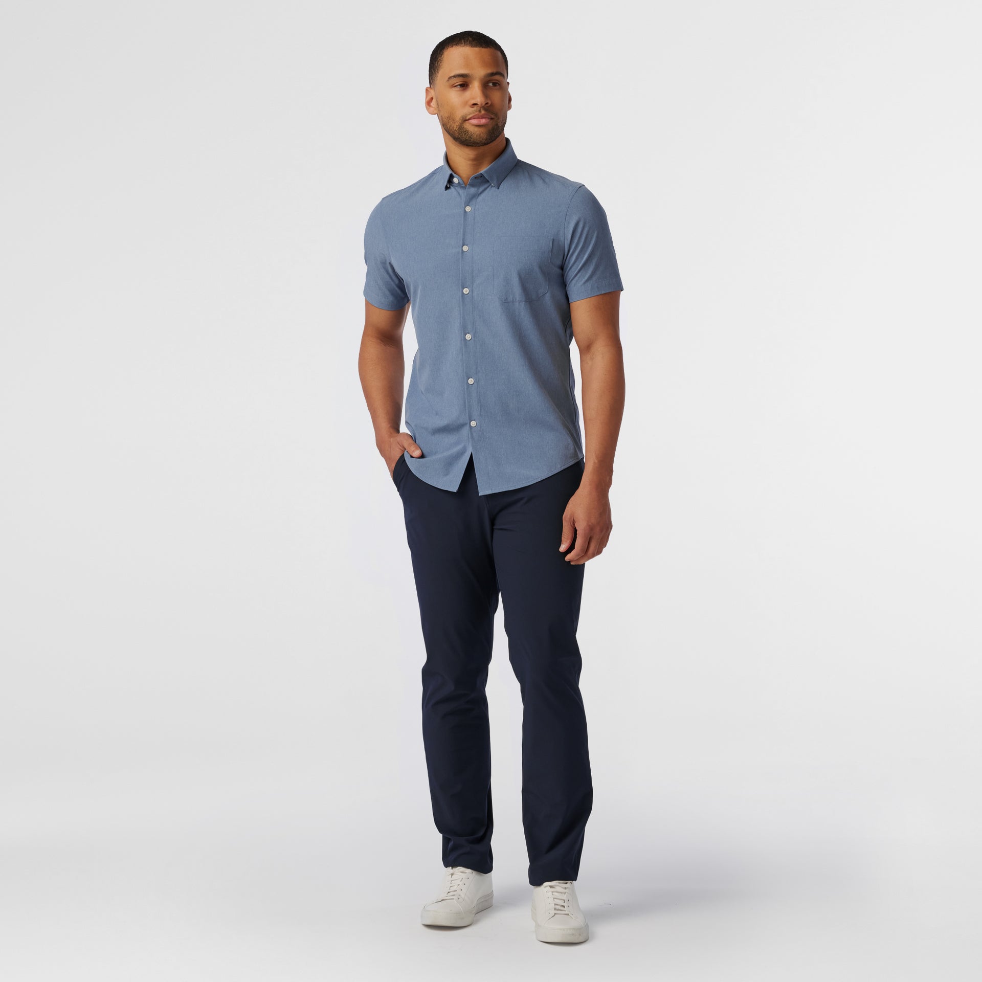 Model wearing the Mizzen+Main Leeward Short Sleeve Dress Shirt (Trim Fit) in Coastal Fjord Heather (chambray blue), showing the tailored fit and spread collar.