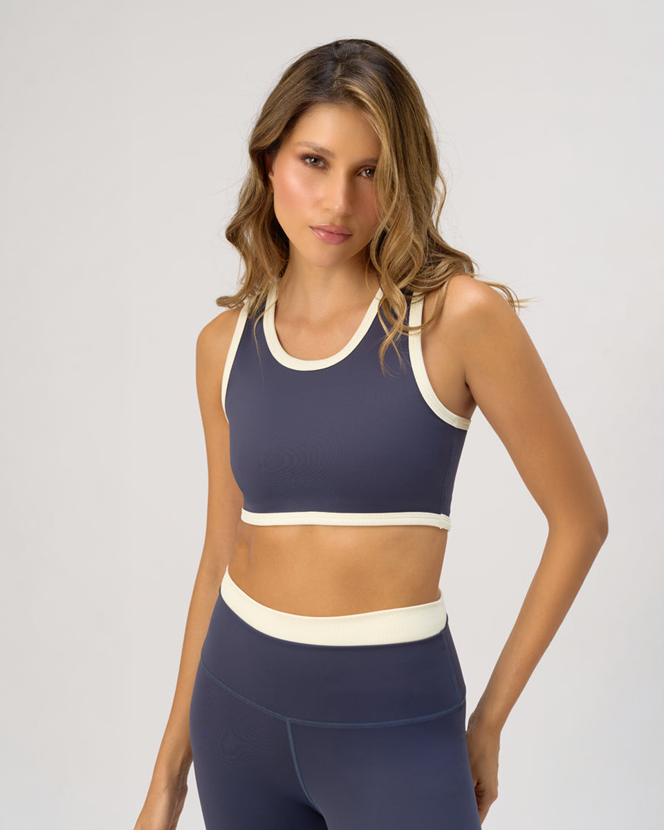 Woman wearing a navy sports bra and leggings with white accents on a light gray background
