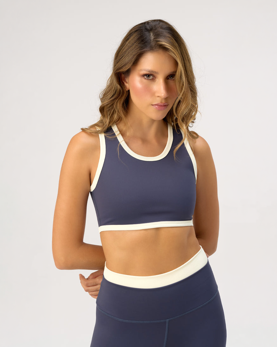 Woman wearing a navy sports bra and leggings with white trim on a light gray background