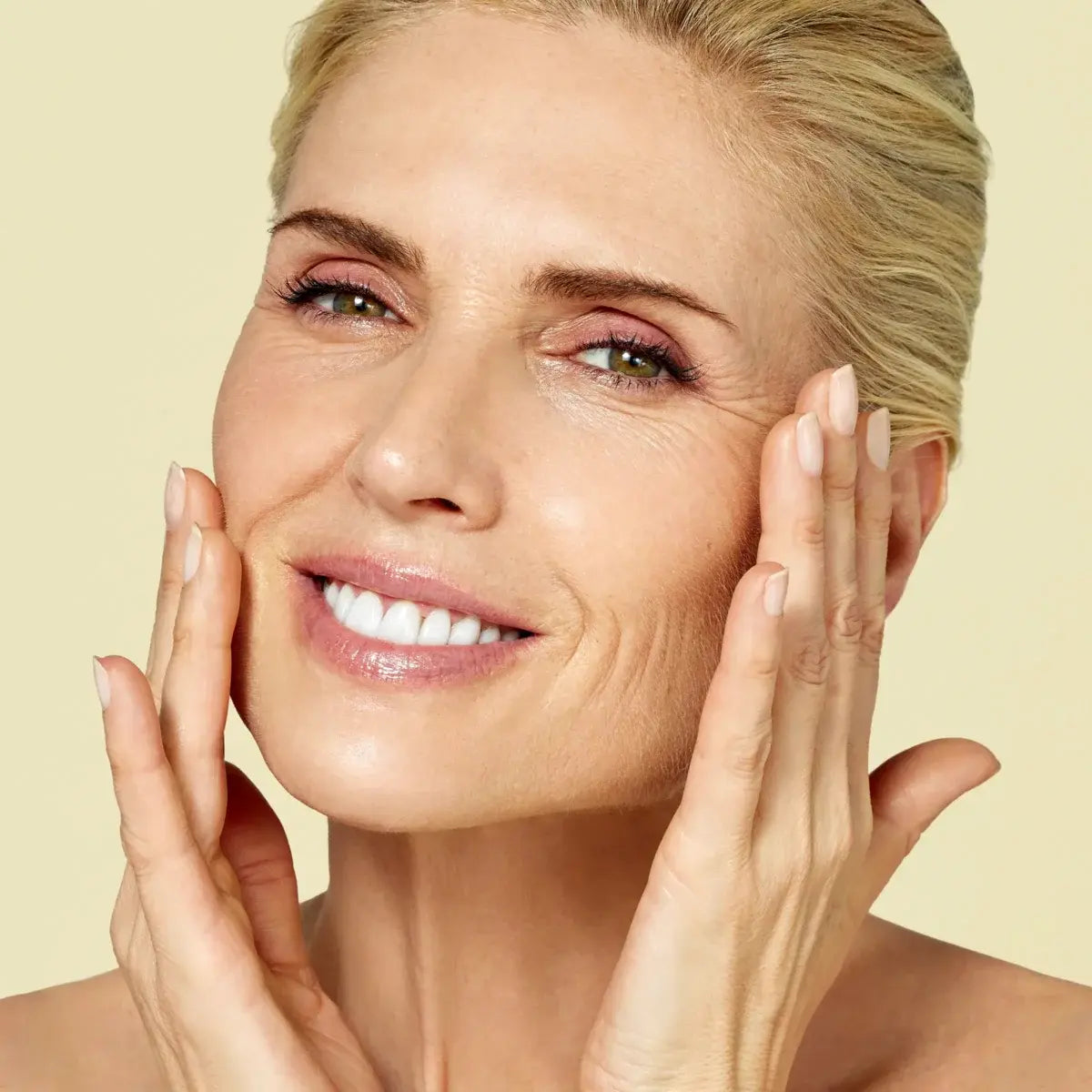Close up of smiling, middle-aged woman applying ISDINCEUTICS Melatonik overnight recovery serum to her face to boost vitality and elasticity. 