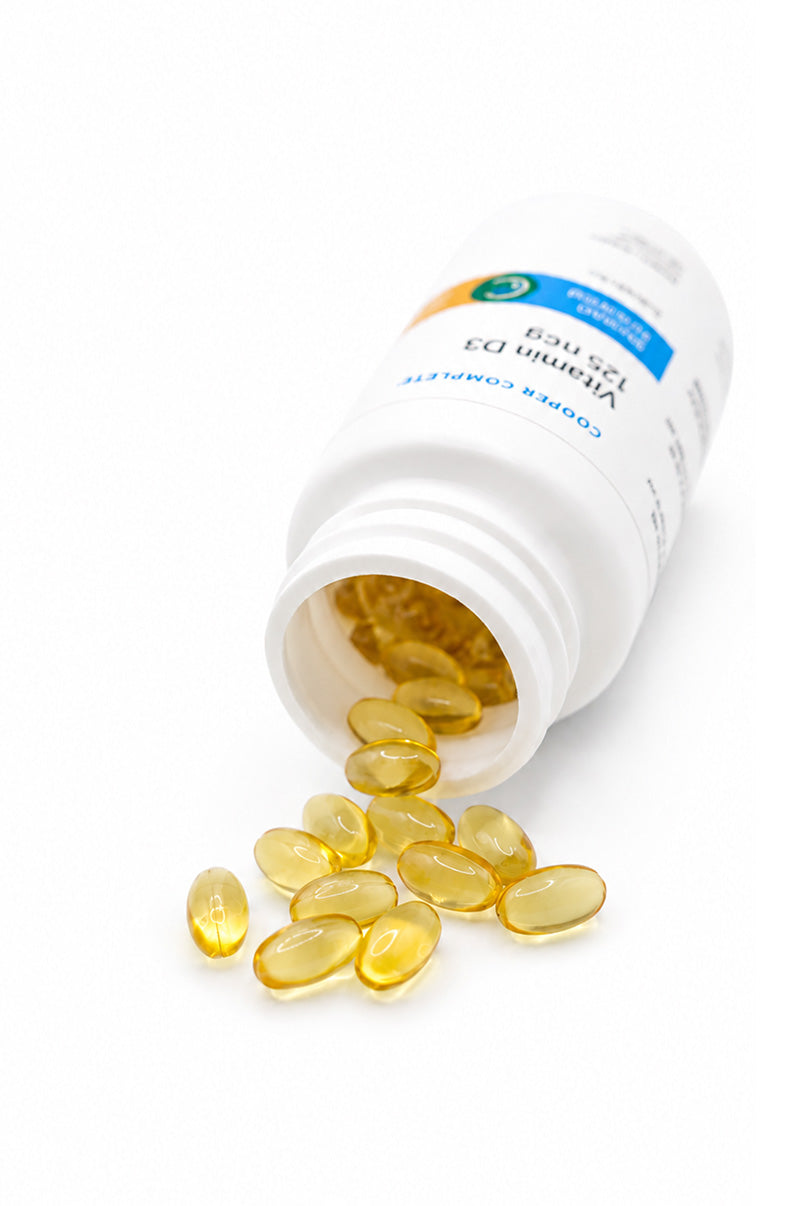 Open white Cooper Complete Vitamin D3 125 mcg (5000 IU) Supplement pill bottle with softgels spilling out on a white background