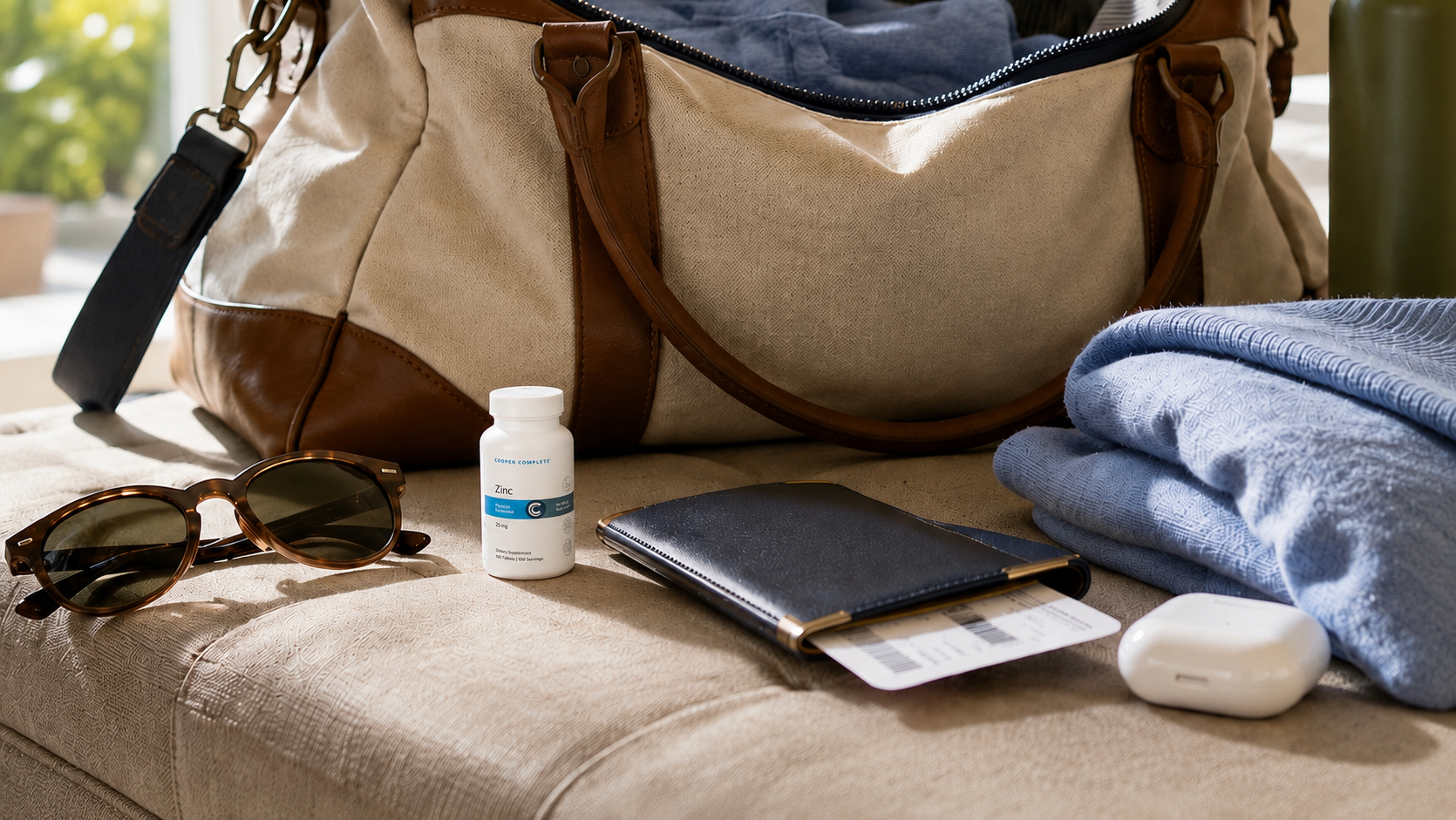 A bottle of Cooper Complete Zinc displayed with travel essentials, including a weekender duffle bag, passport, sunglasses, and folded clothing for everyday wellness on the go.