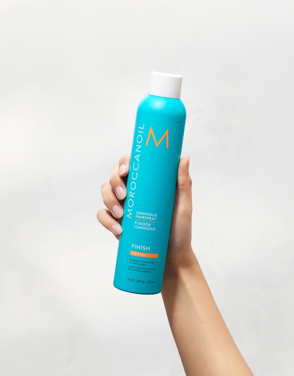 Moroccanoil Luminous Hairspray Strong 330 mL turquoise aerosol can held upright in hand, product lifestyle view.